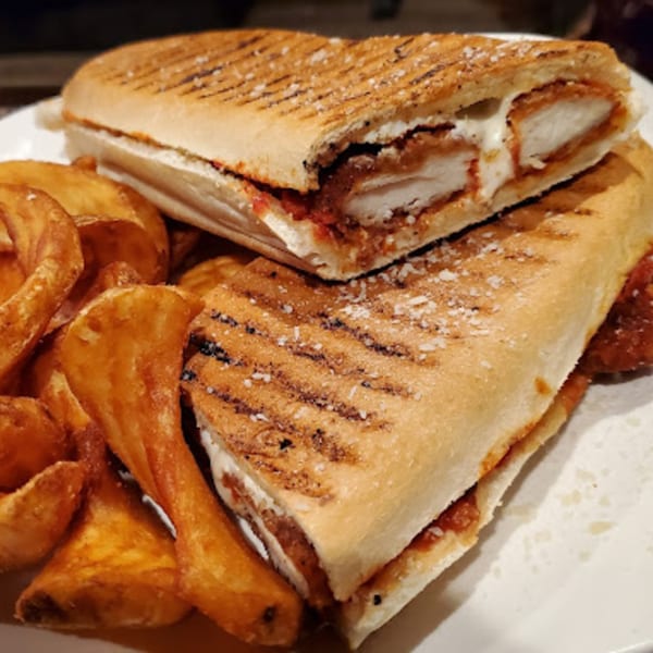 Chicken parmesan panini with melted cheese and sauce, served with golden potato wedges.