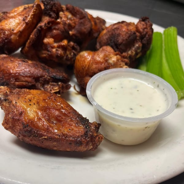 Crispy brown chicken wings with a side of ranch dressing and celery sticks on a white plate.
