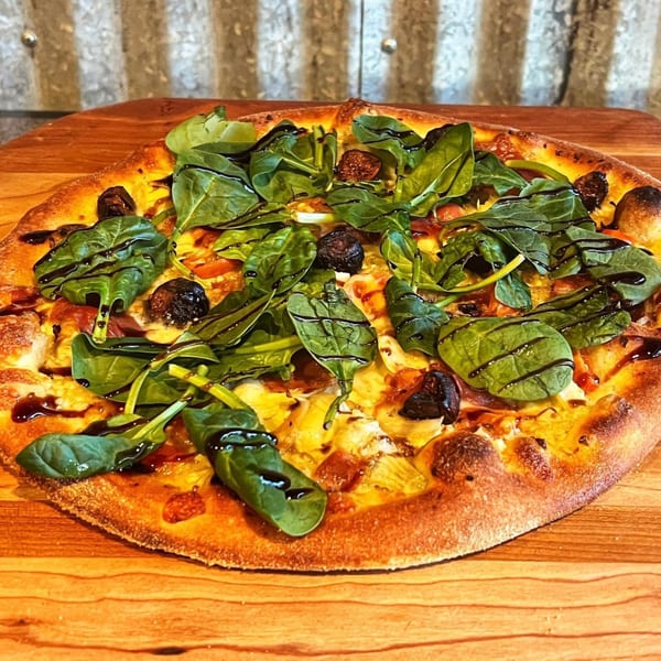 Pizza Rock pizza with spinach, figs, and balsamic glaze on a wooden board.