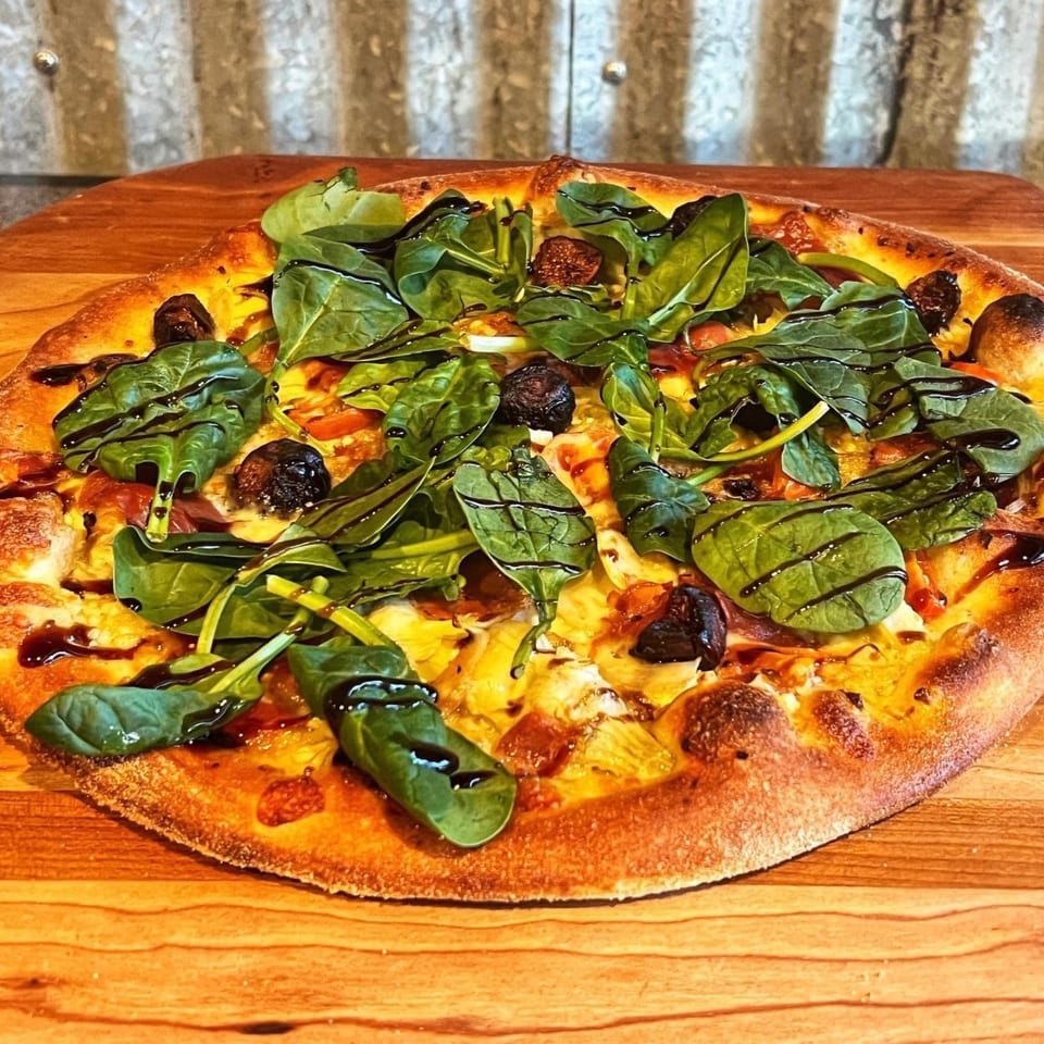 Pizza Rock pizza with spinach, figs, and balsamic glaze on a wooden board.