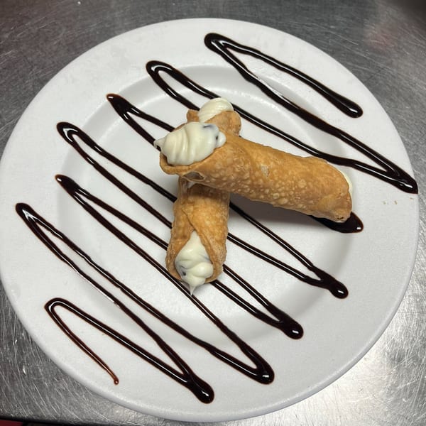 Two cannolis filled with white cream and chocolate chips, drizzled with chocolate sauce on a white plate.