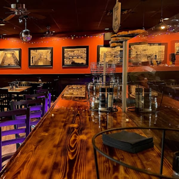 Pizza Rock's dining area with a long wooden bar, purple chairs, and framed pictures on orange walls.