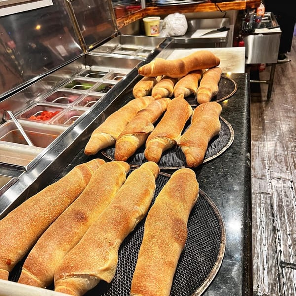 Freshly baked breadsticks on metal cooling racks next to a pizza topping station at Pizza Rock.