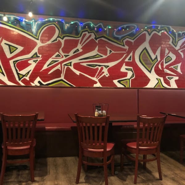 Red booths and chairs in a Pizza Rock dining area with a colorful graffiti mural on the brick wall.