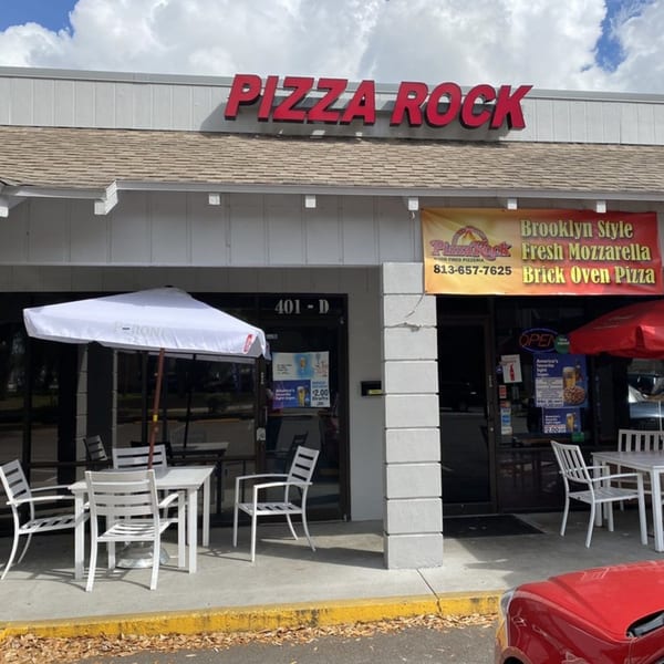 The exterior of Pizza Rock restaurant with outdoor seating under white and red umbrellas.