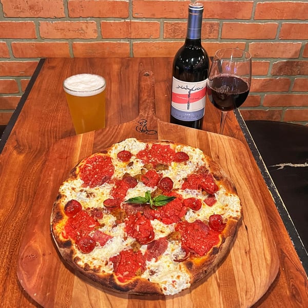 Pizza Rock's pepperoni pizza with a bottle of red wine and a glass of beer on a wooden table.