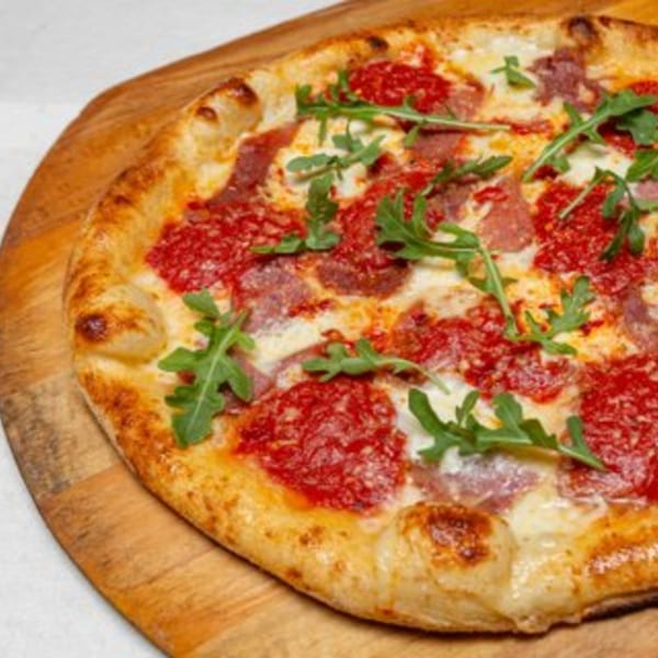 Pizza Rock's pizza with red sauce, cheese, pepperoni, and fresh arugula on a wooden board.