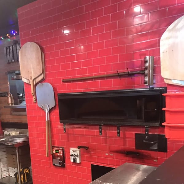Pizza Rock's red tiled wall with a pizza oven, peels, and cooking tools.