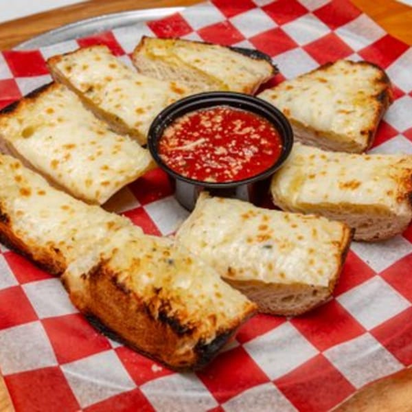 Cheesy garlic breadsticks with a side of marinara sauce on red and white checkered paper.